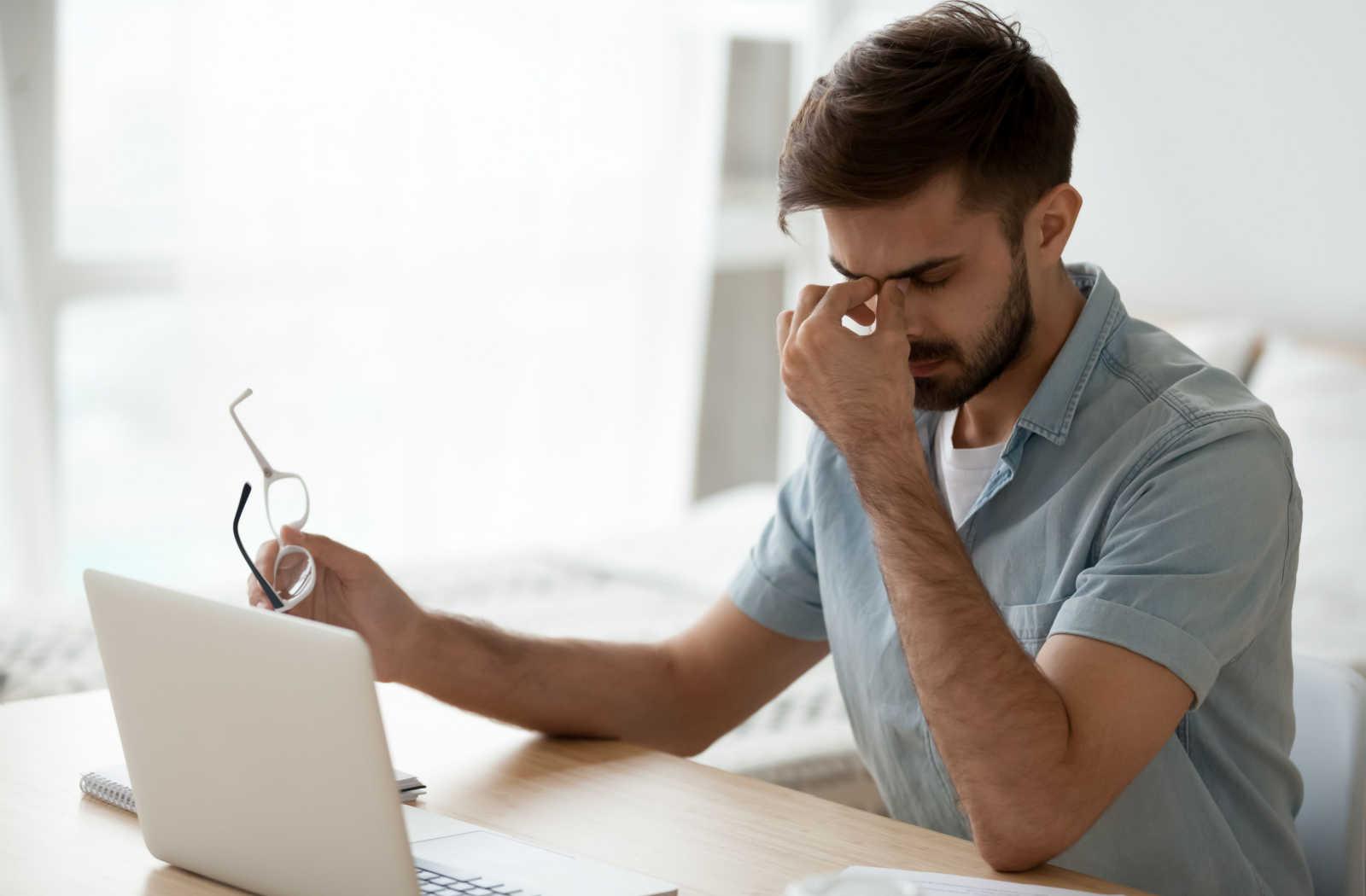 A man rubbing his eyes while working on a laptop.